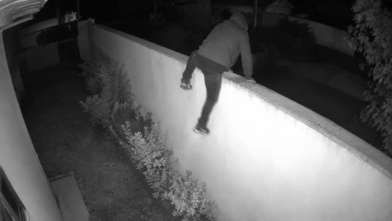 Câmera 1: pessoa encapuzada escalando o muro do perímetro