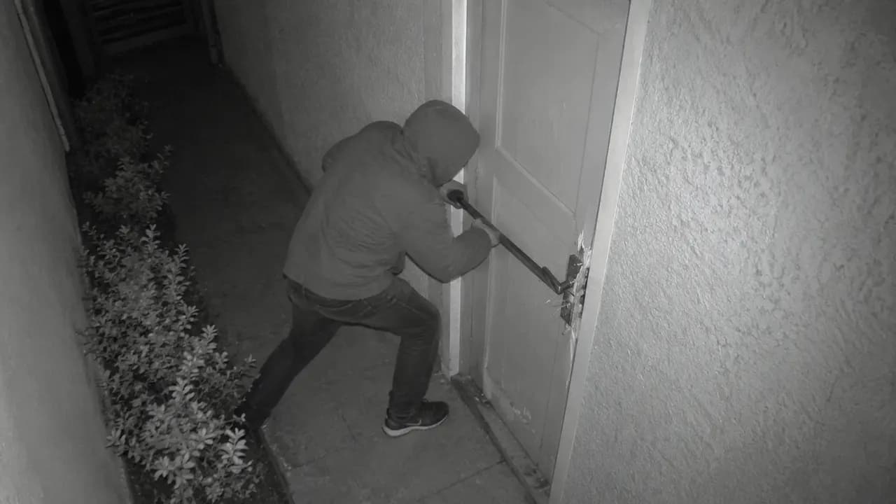 Câmera 2: pessoa encapuzada arrombando a porta de serviço com pé de cabra